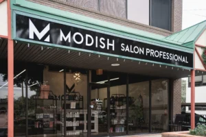 A storefront with a sign that reads "Modish Salon Professional" above large windows displaying hair and beauty products inside. - Modish Salon Professional